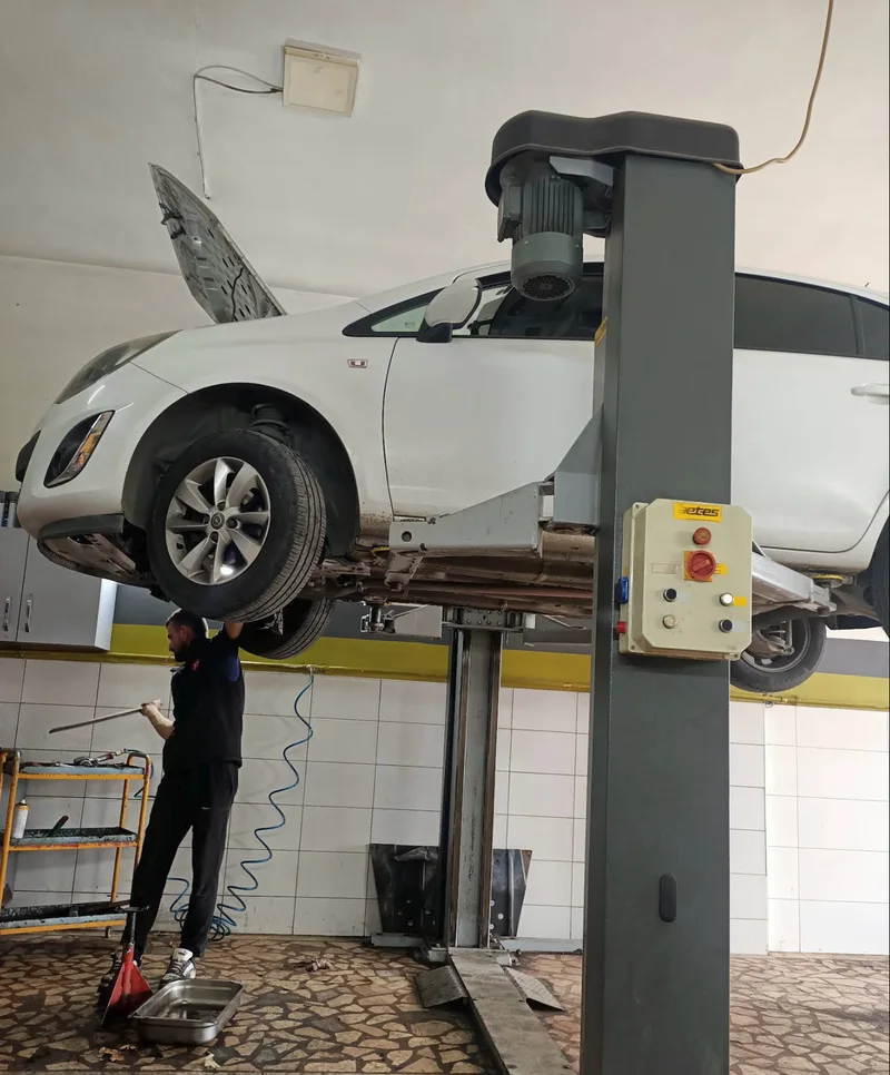 Atölyede lift üzerindeki araç ve araç altında çalışan usta